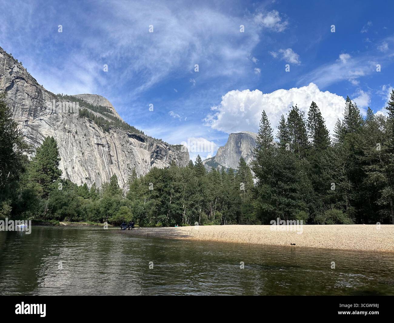 A scenic view of Half Dome mountain with pine trees and a calm river under a bright blue sky at Yosemite National Park. - Smartphone Captured Stock Image