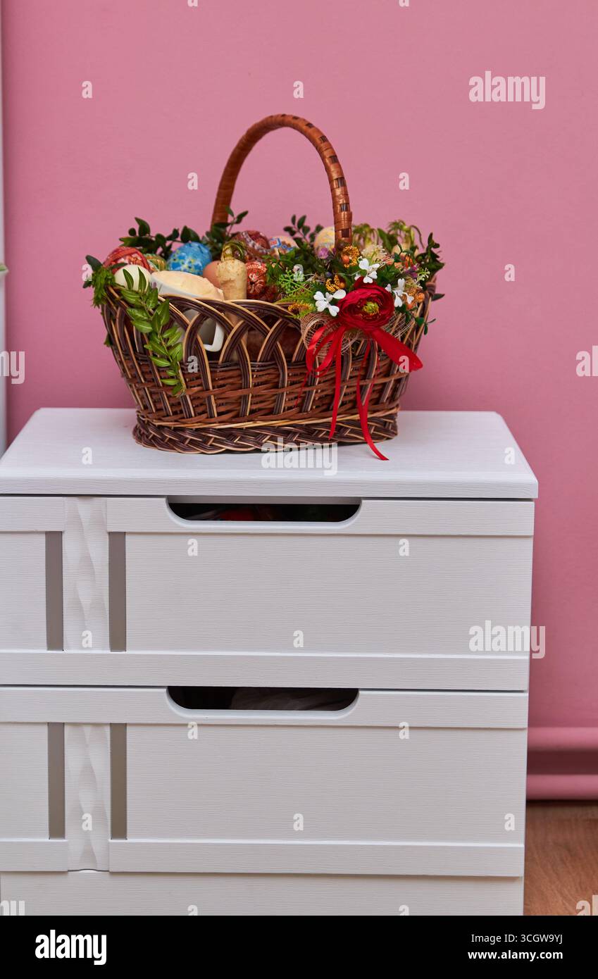 decorated Easter basket with easter and Easter eggs and sausage on a white bedside table Stock Photo