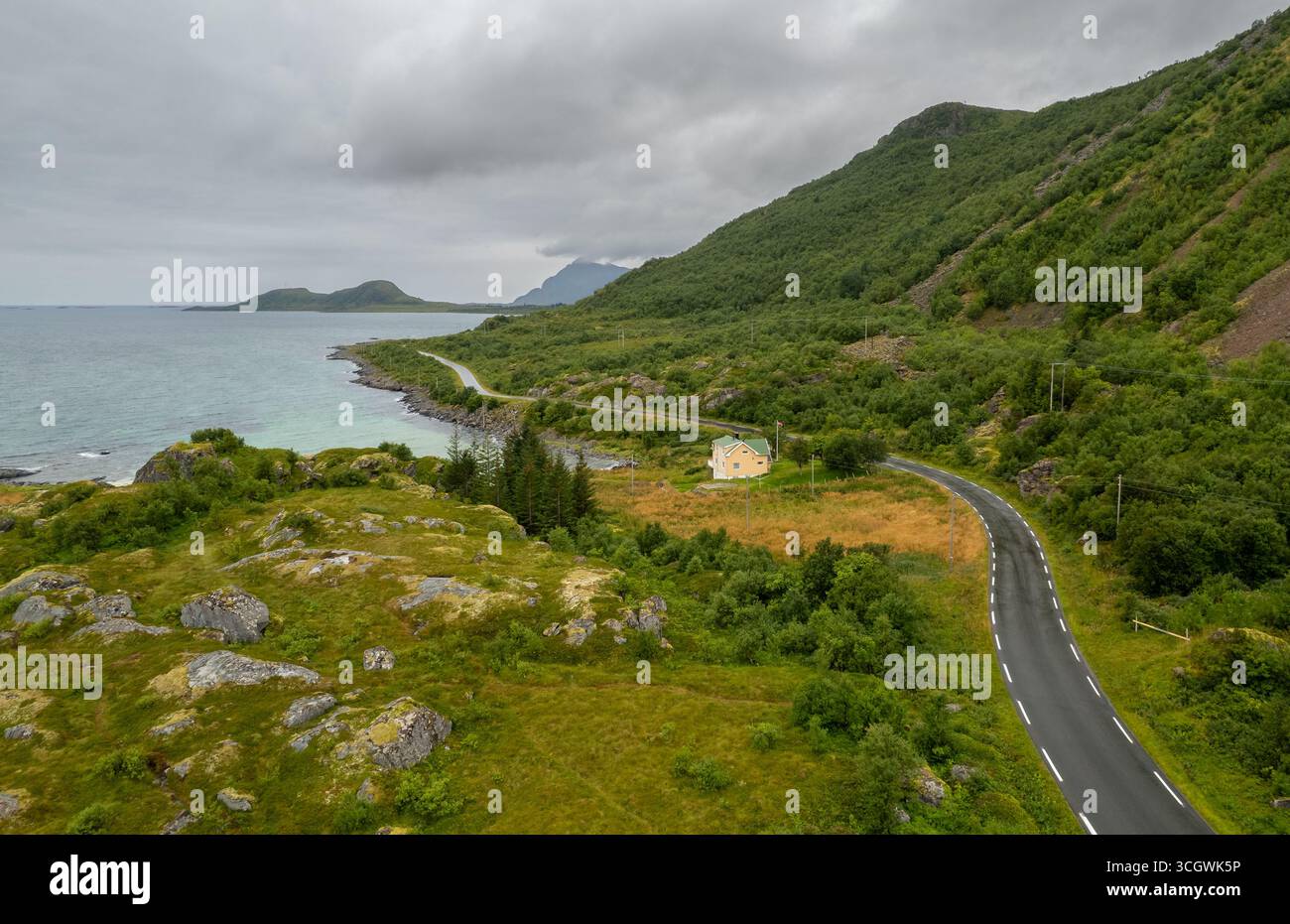 Aerial drone view of a scenic road in Lofoten, Norway, with yellow cabin house at the edge of the lake. Stock Photo