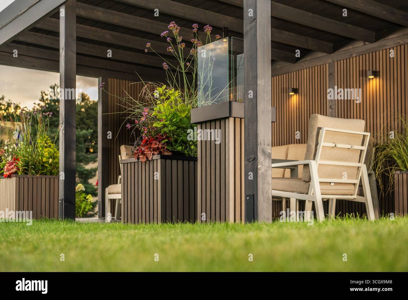 A cozy outdoor seating area features comfortable chairs and vibrant plants, ideal for relaxation in a garden during sunset. Stock Photo