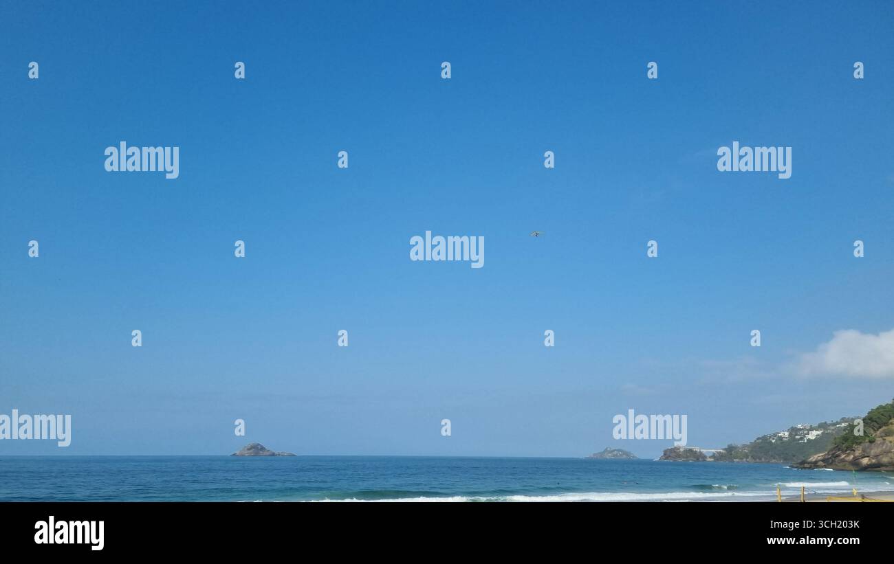 An open expanse of blue sky meets the calm ocean, with gentle waves forming a soft line along the horizon. - Smartphone Captured Stock Image