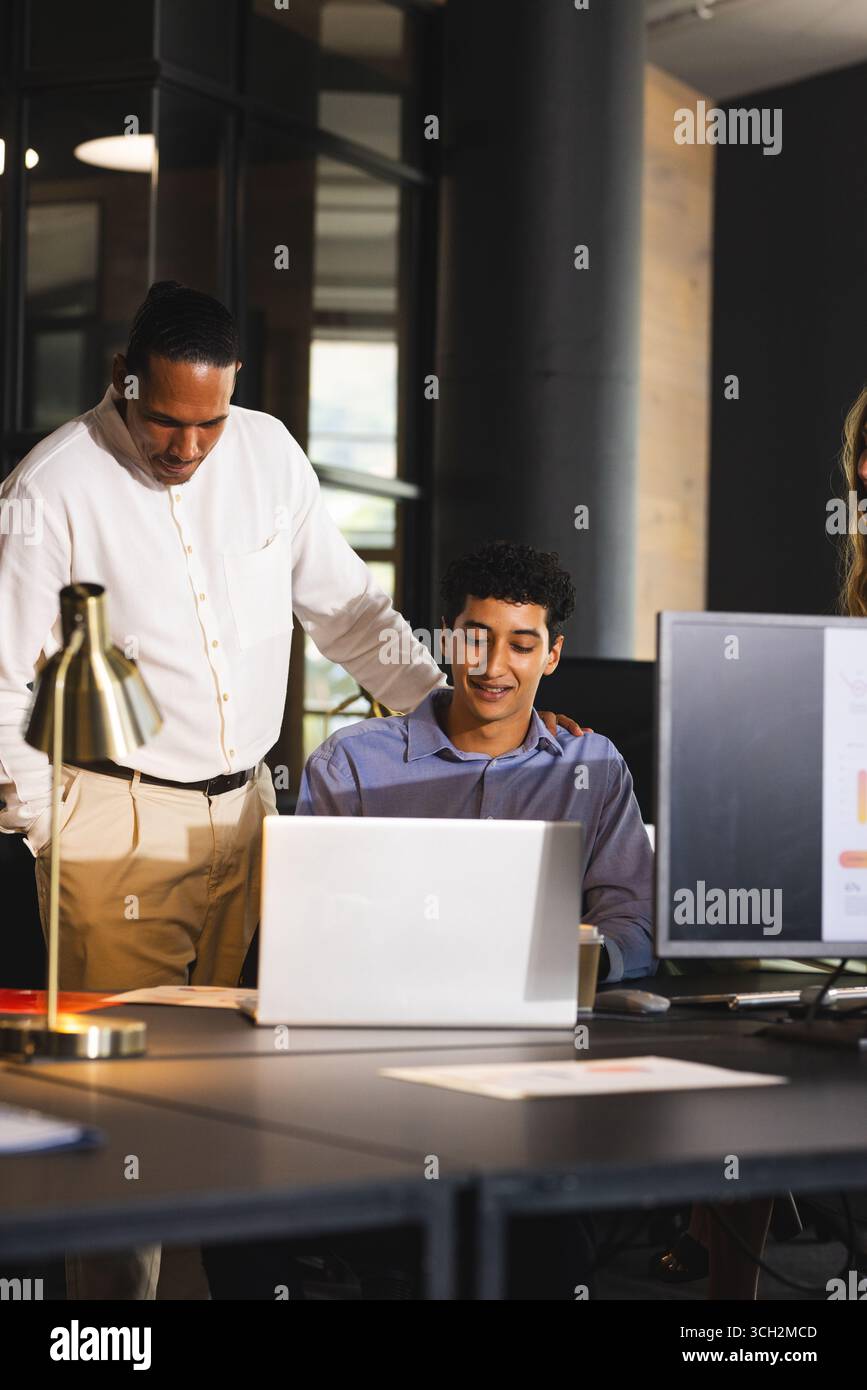 Collaborating on laptop, business diverse professionals discussing project details in modern office Stock Photo