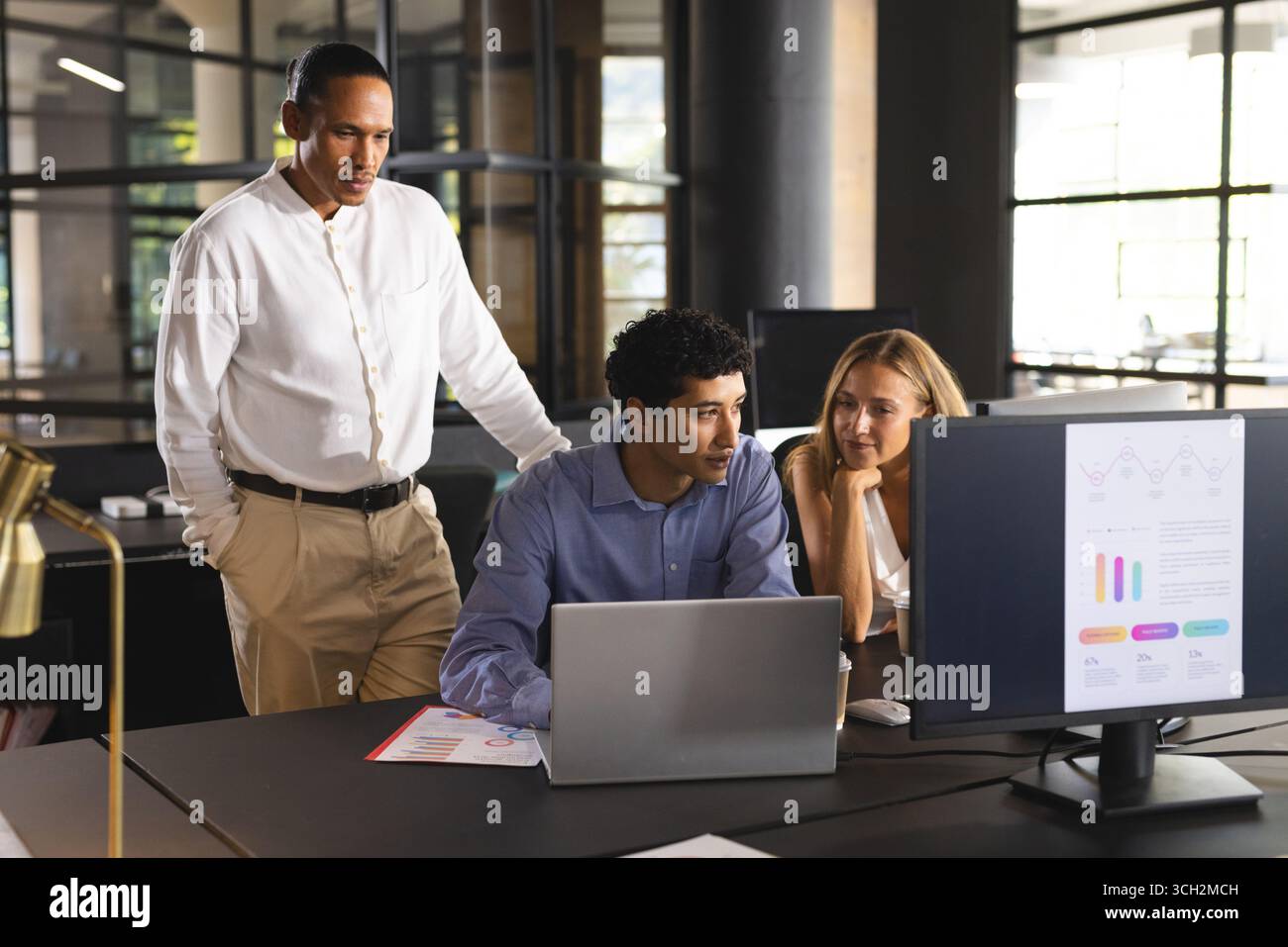 Diverse team collaborating on project, using laptops and discussing data in modern office Stock Photo