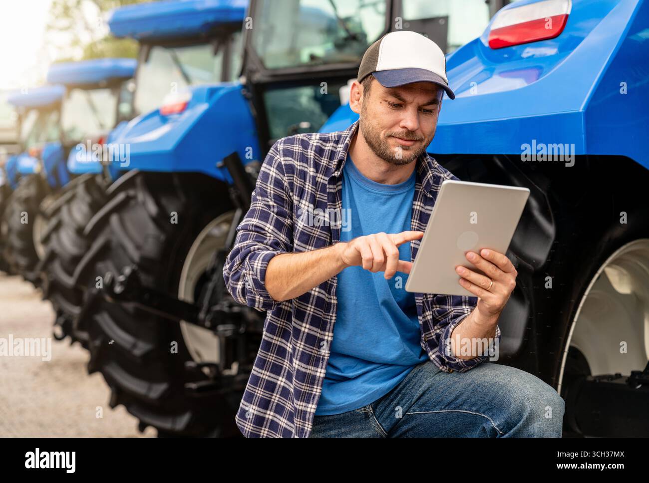 Man farm worker using digital tablet standing neat tractor outdoors Stock Photo