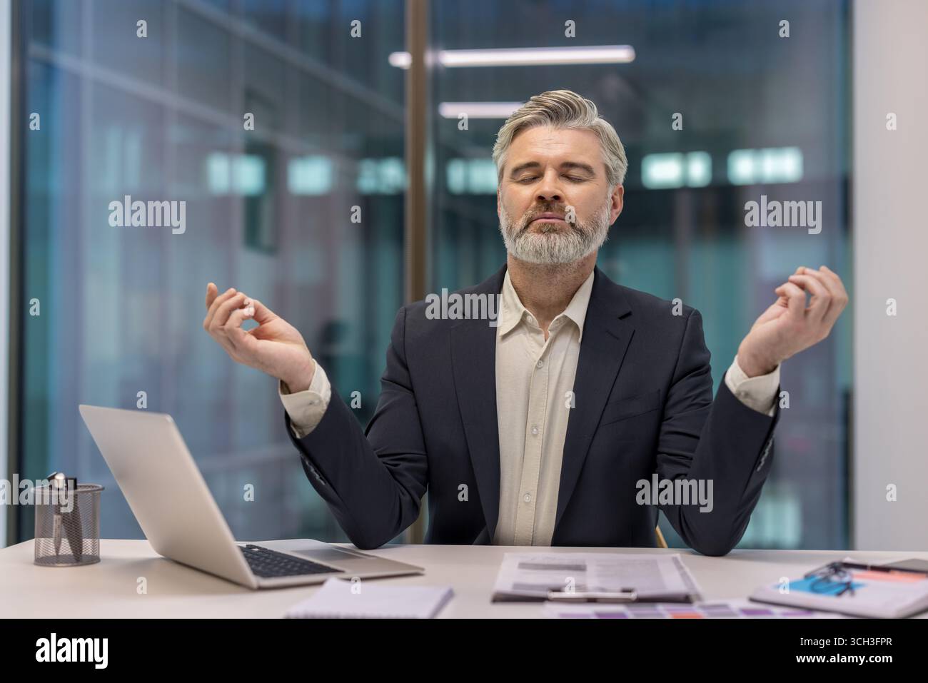 Office employee practicing mindfulness meditation at their desk to achieve peace and focus in work environments. Demonstrating balance, calmness, and relaxation as a part of stress management Stock Photo