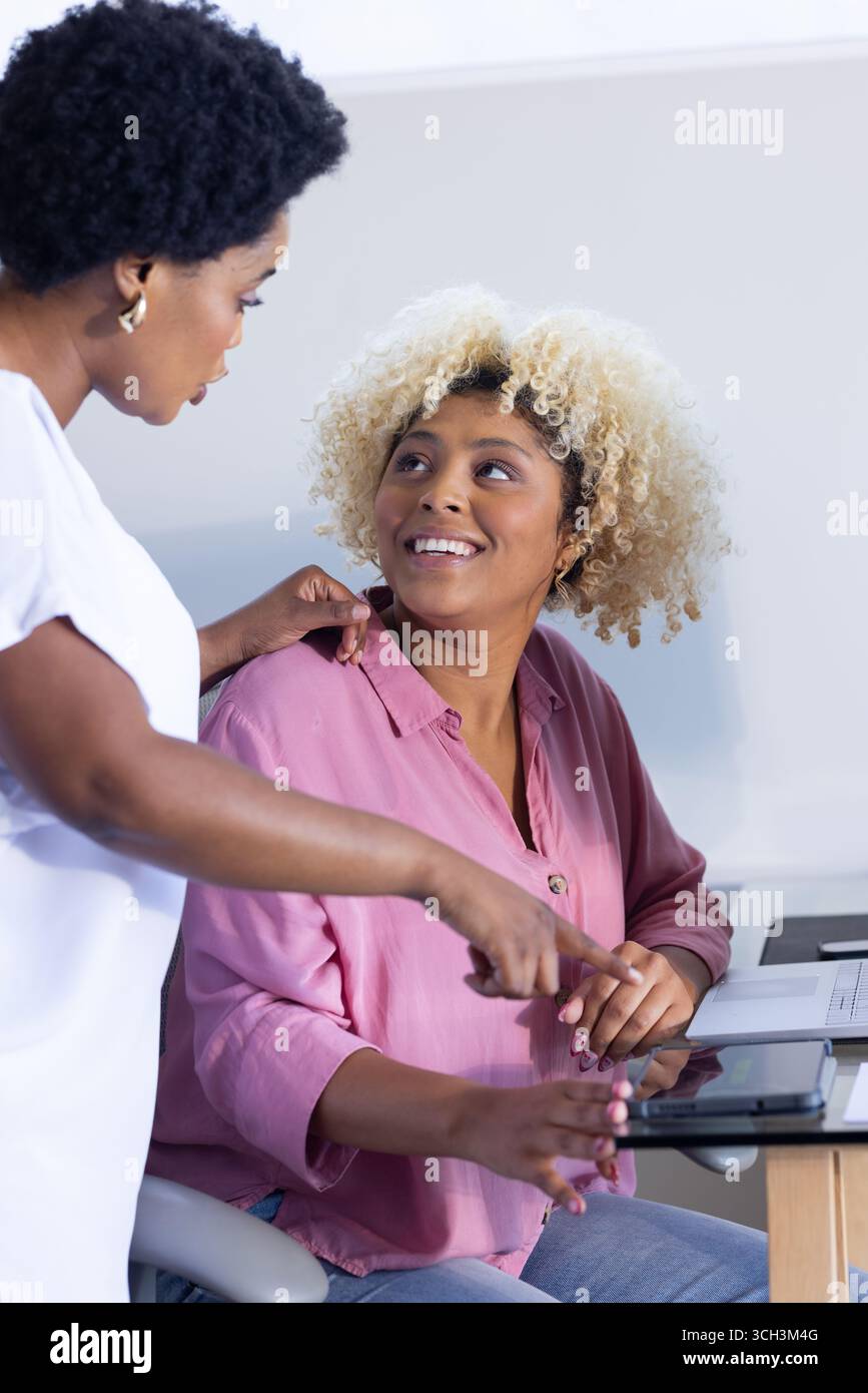 Two women collaborating at desk, using tablet and smiling in office Stock Photo
