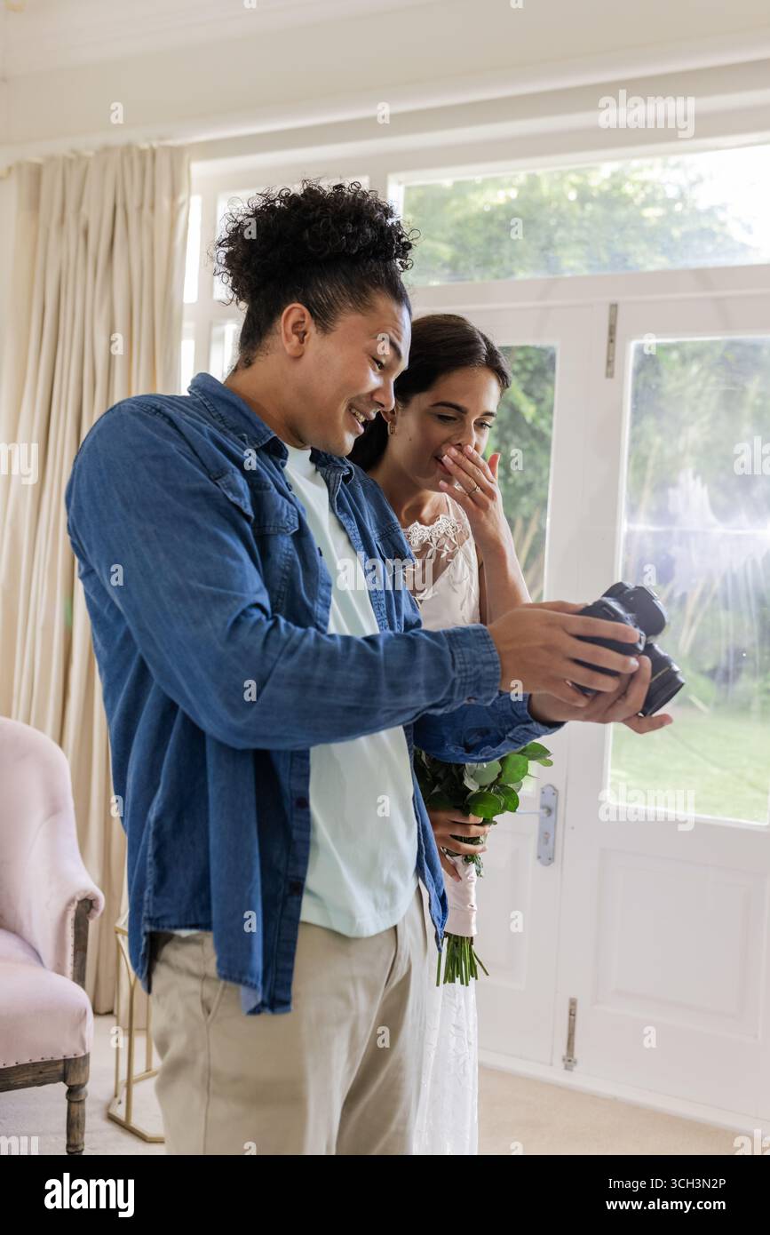 Bride and groom joyfully reviewing wedding photos together at home Stock Photo