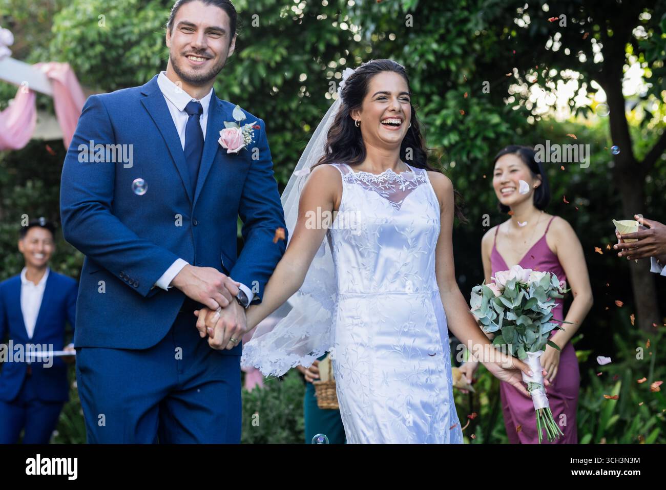 Bride and groom walking joyfully down aisle, surrounded by smiling guests Stock Photo