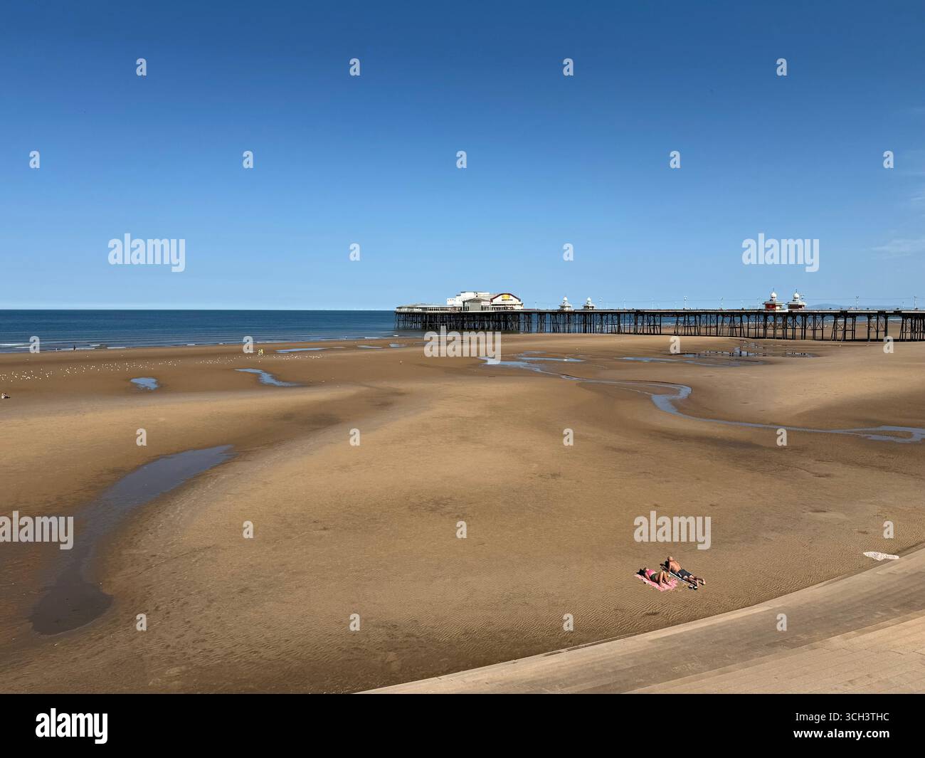 Blackpool beach and North Pier at low tide. Two people sunbathing on empty beach. - Smartphone Captured Stock Image