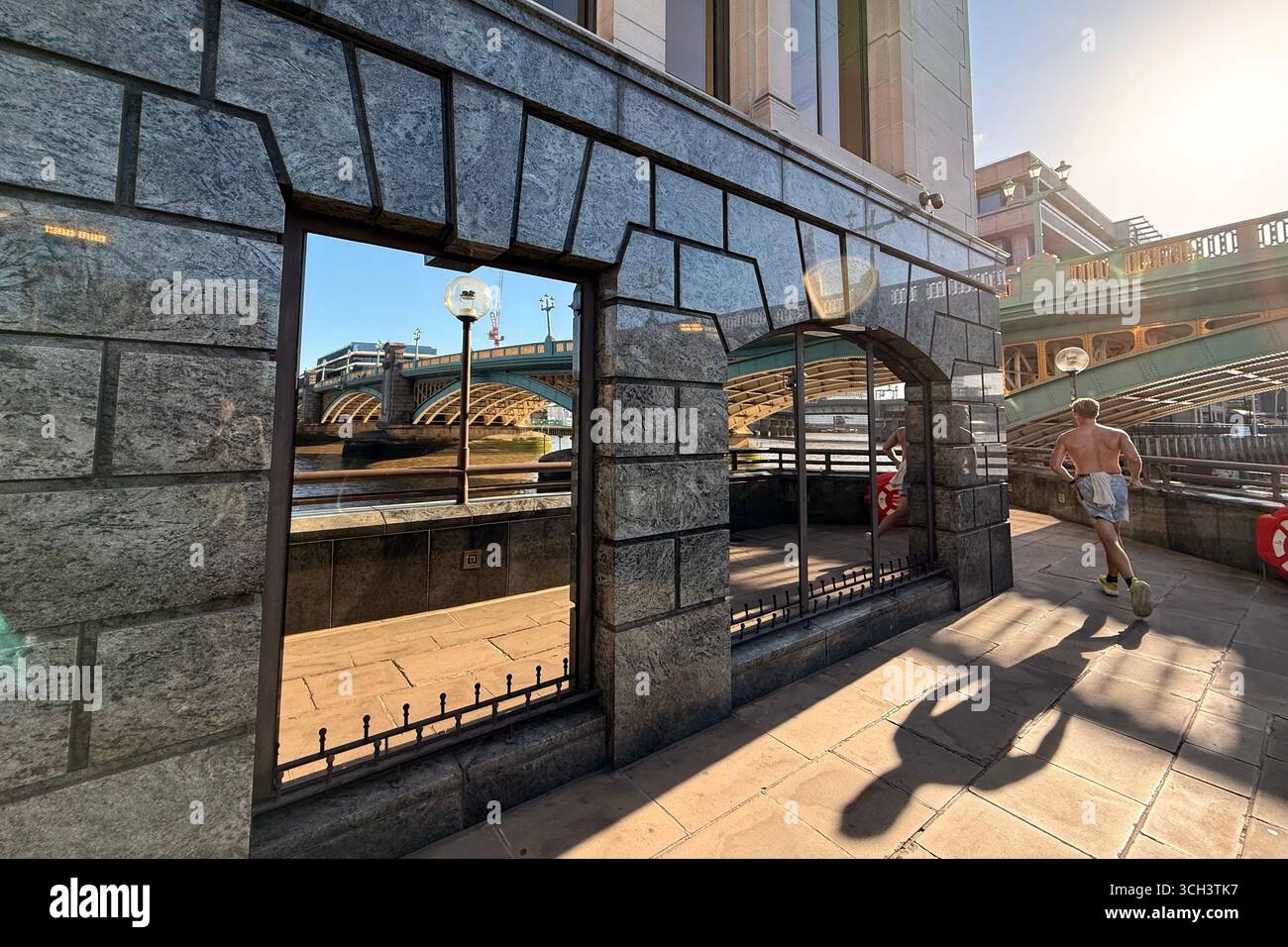 Southwark bridge over Thames in central London. Bridge and river reflected in windows with runner passing casting a long shadow early in morning. - Smartphone Captured Stock Image