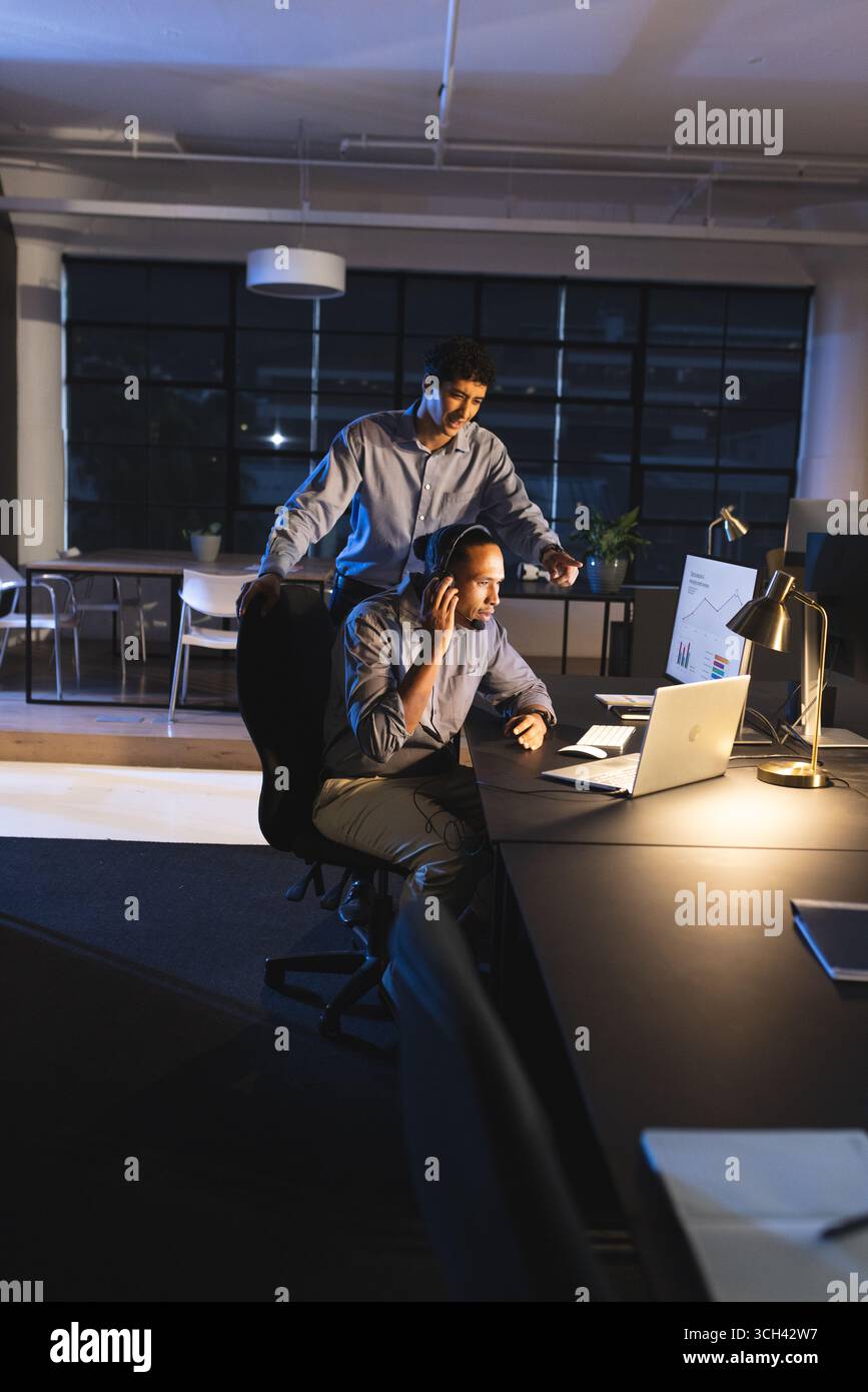 Businessmen working late in office, discussing project on laptop with focus Stock Photo