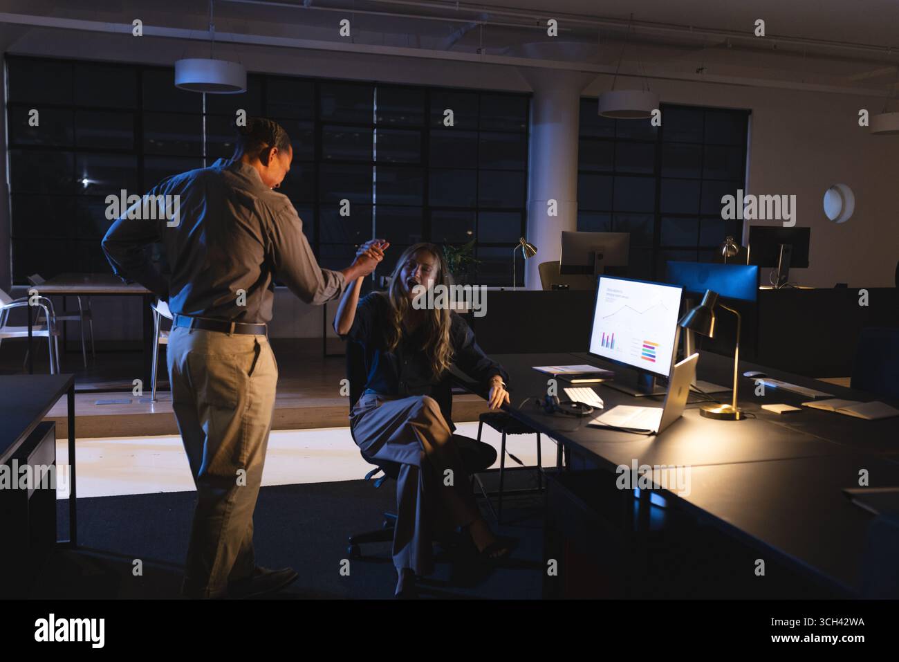 Colleagues discussing project in office at night, analyzing data on computer screen Stock Photo