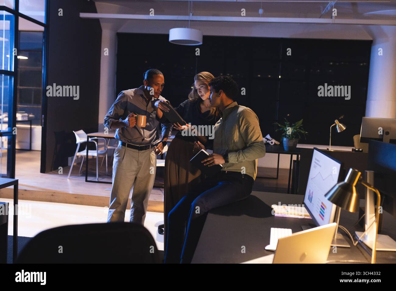 Business professionals discussing project details in modern office during late hours Stock Photo