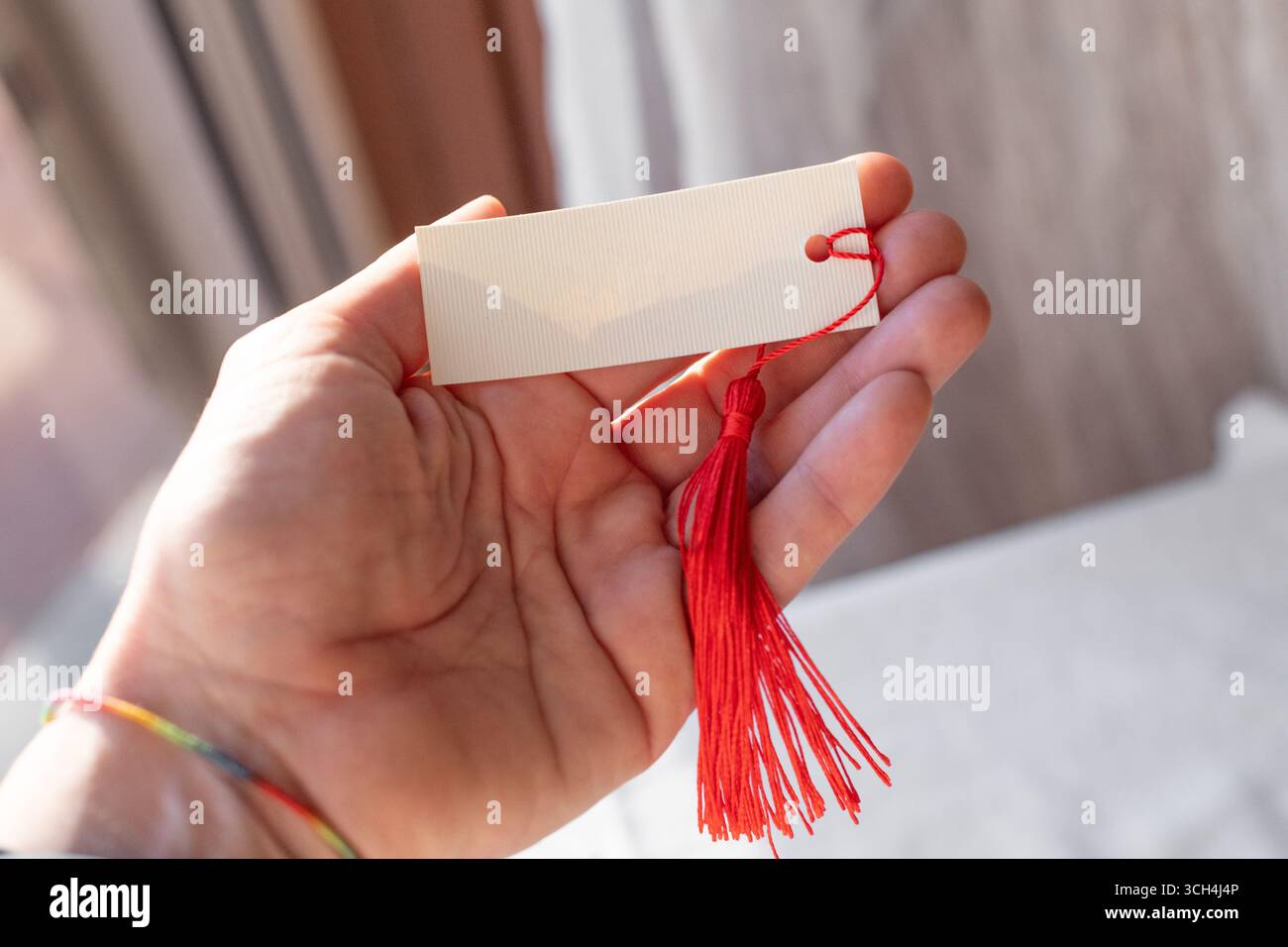 Handheld Blank Card Mockup With Red Tassel in Natural Light Stock Photo