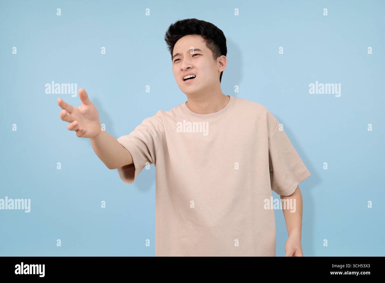 A man gestures with hands implying irritation or rejection, posing against a neutral blue backdrop Stock Photo