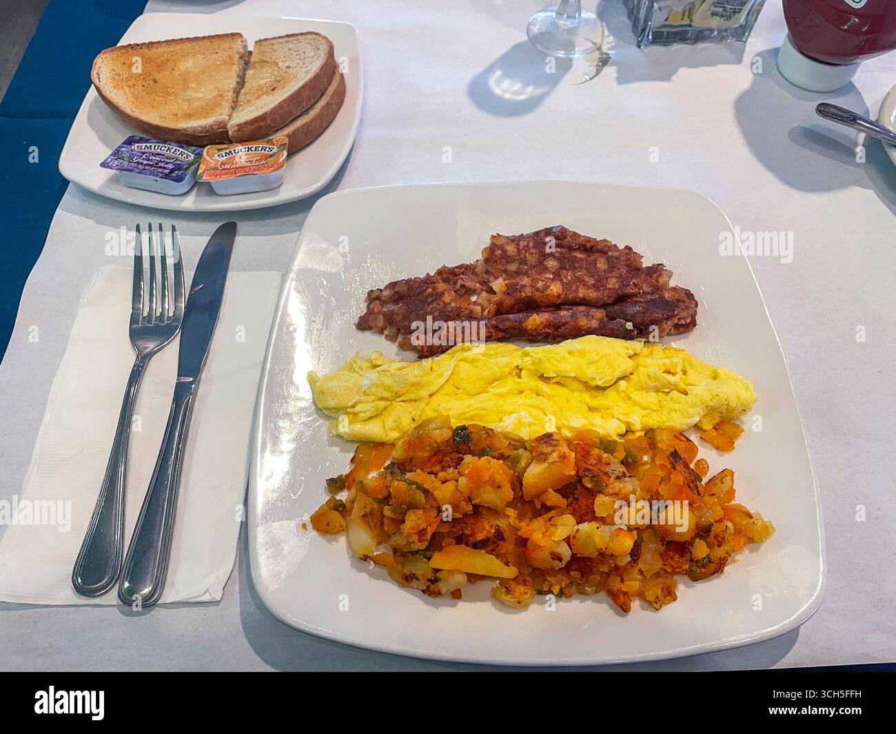 Classic breakfast plate with fluffy scrambled eggs, crispy corn beef hash, and golden home fries, served with toasted bread, butter, and jam on the si Stock Photo