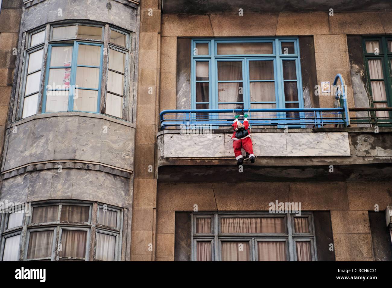 Porto, Portugal - 12.25.2022: A cheerful Santa figure perched on a charming balcony in a vibrant urban cityscape setting Stock Photo