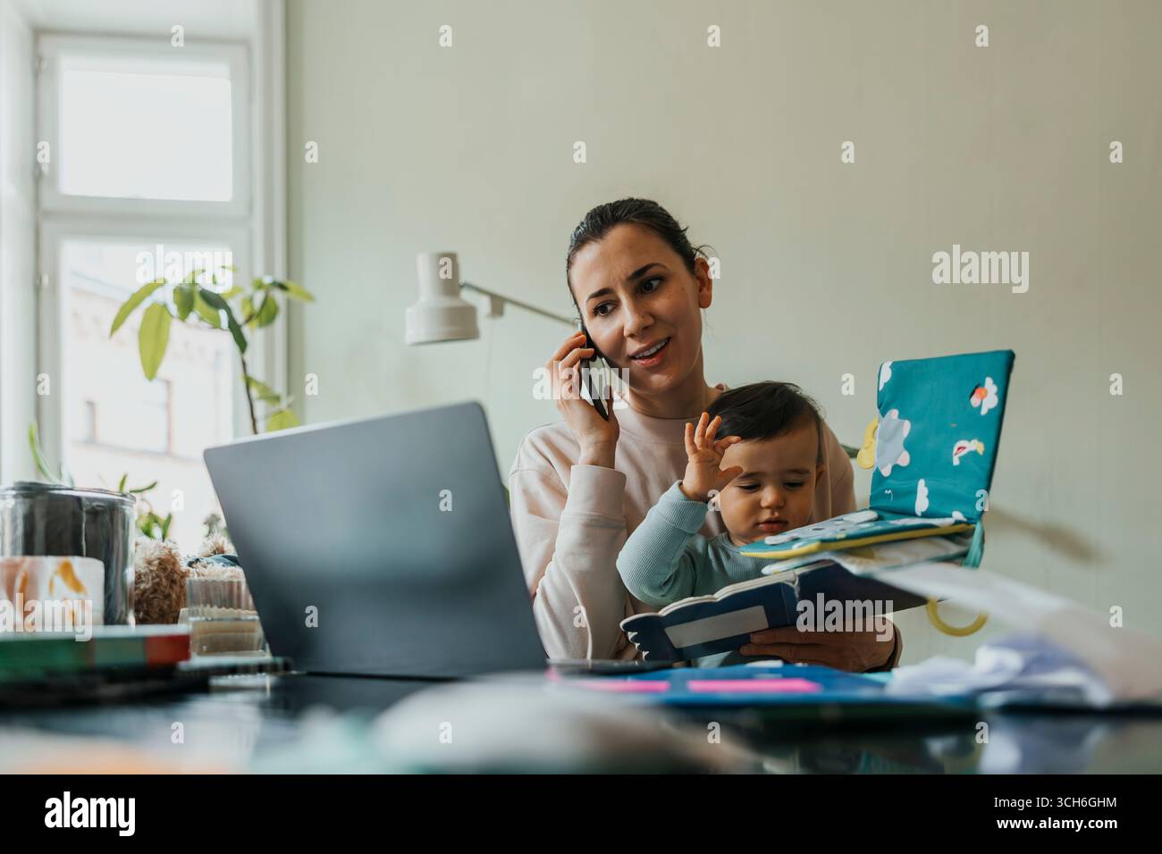 Female freelancer working with wireless technologies while holding son at home Stock Photo