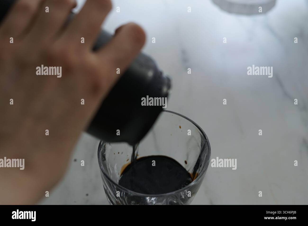 Gently Pouring the Dark Liquid into a Clear Glass on Marble Surface Stock Photo