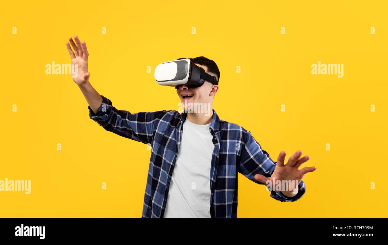 Joyful young guy using virtual reality headset, controlling cyber environment with moving gestures on orange background Stock Photo