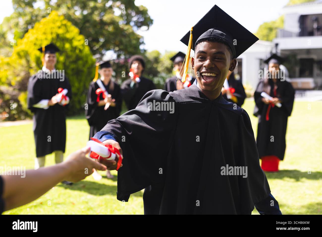 Graduate in cap and gown celebrating in garden, receiving diploma with ...