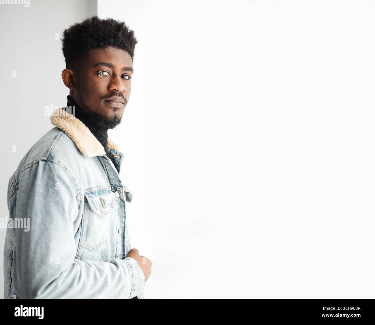 Serious young bearded guy in jeans jacket looking at camera Stock Photo