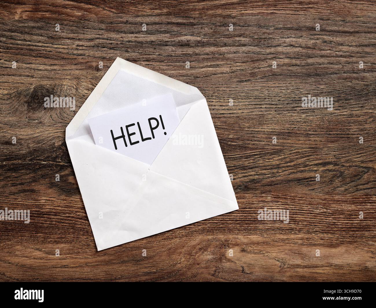 Open envelope containing a card with the word help written on it, lying on a wooden surface. Calling for help and support concept. Stock Photo
