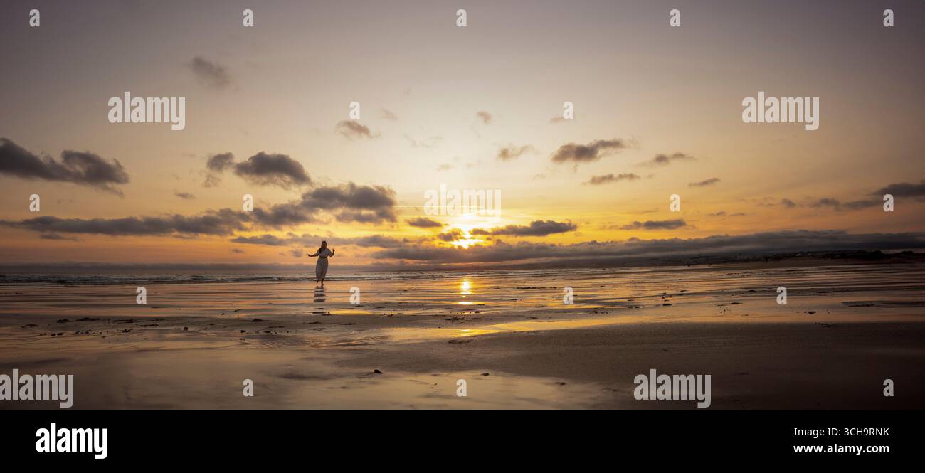 Woman walking on the beach at sunset with cloudy sky Stock Photo
