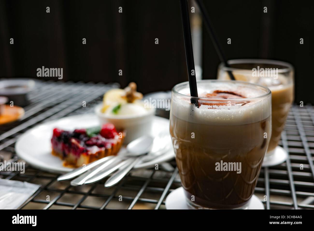 Close-up of iced coffee with cocoa powder topping, served with assorted desserts on a cafe table in Kyoto, Japan.. Stock Photo