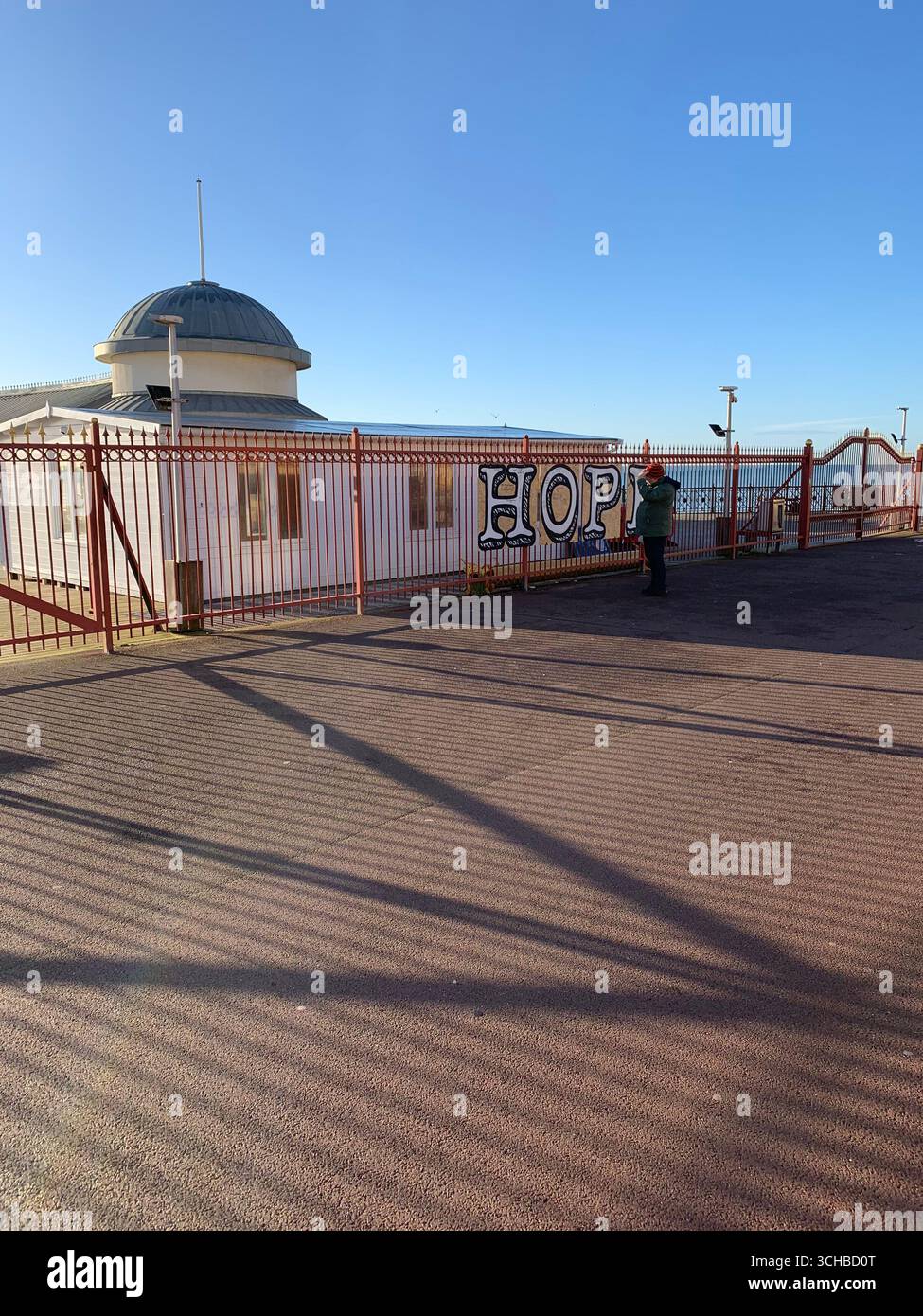 Disconsolate lonely person in front of 'Hope' graffiti on closed-down Hastings pier during Covid lockdown 2020 - Smartphone Captured Stock Image