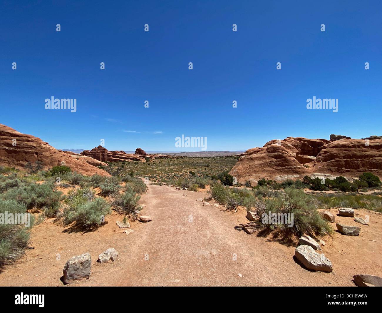 A trail leading through scrub brush and past large rock formations on the Landscape Arch Trail in Arches National Park, Moab, Utah, USA - Smartphone Captured Stock Image