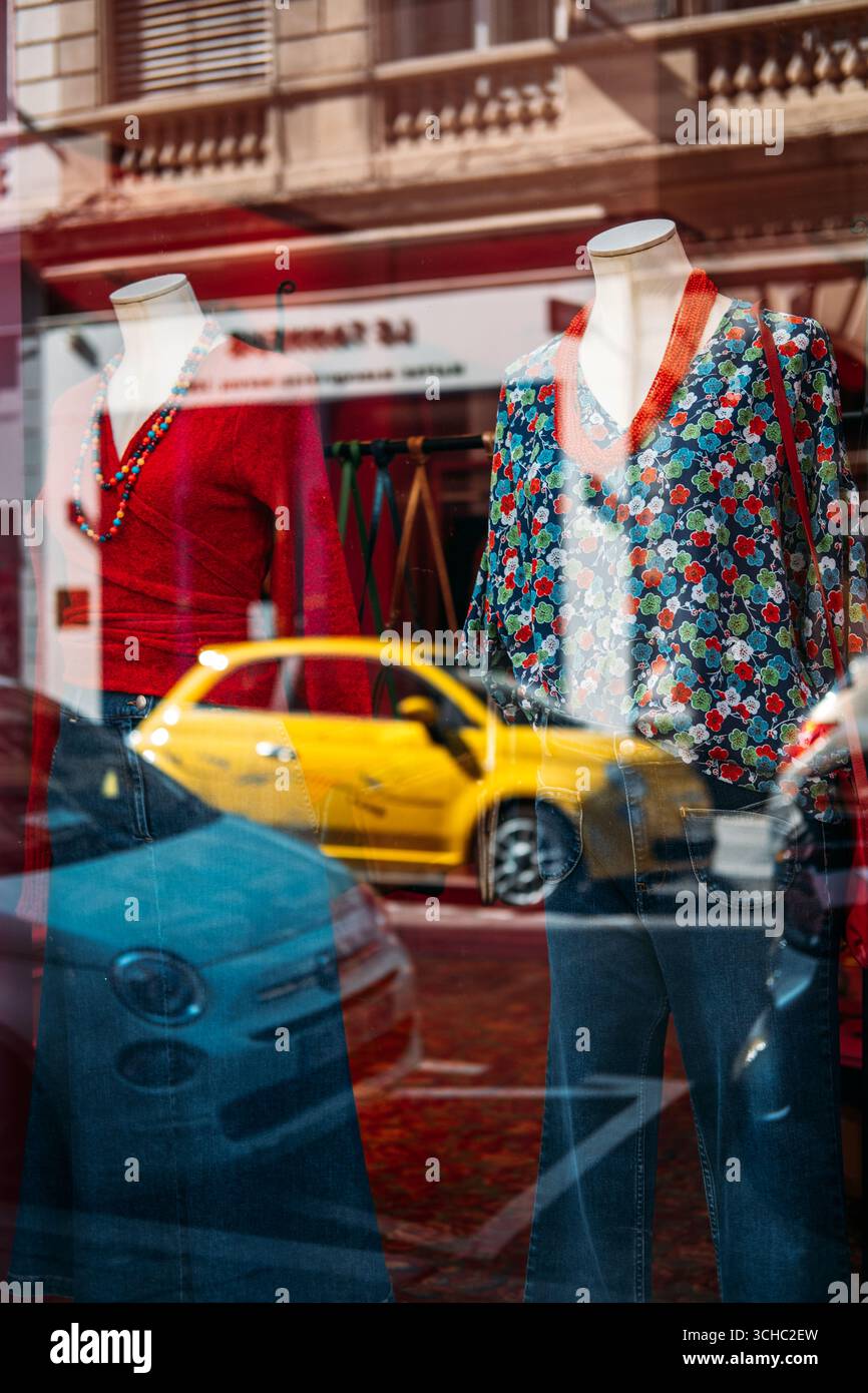 Fashion shop window display with colorful blouses and jeans on mannequins reflecting city street and yellow car in Lyon France August 19 2025 Stock Photo