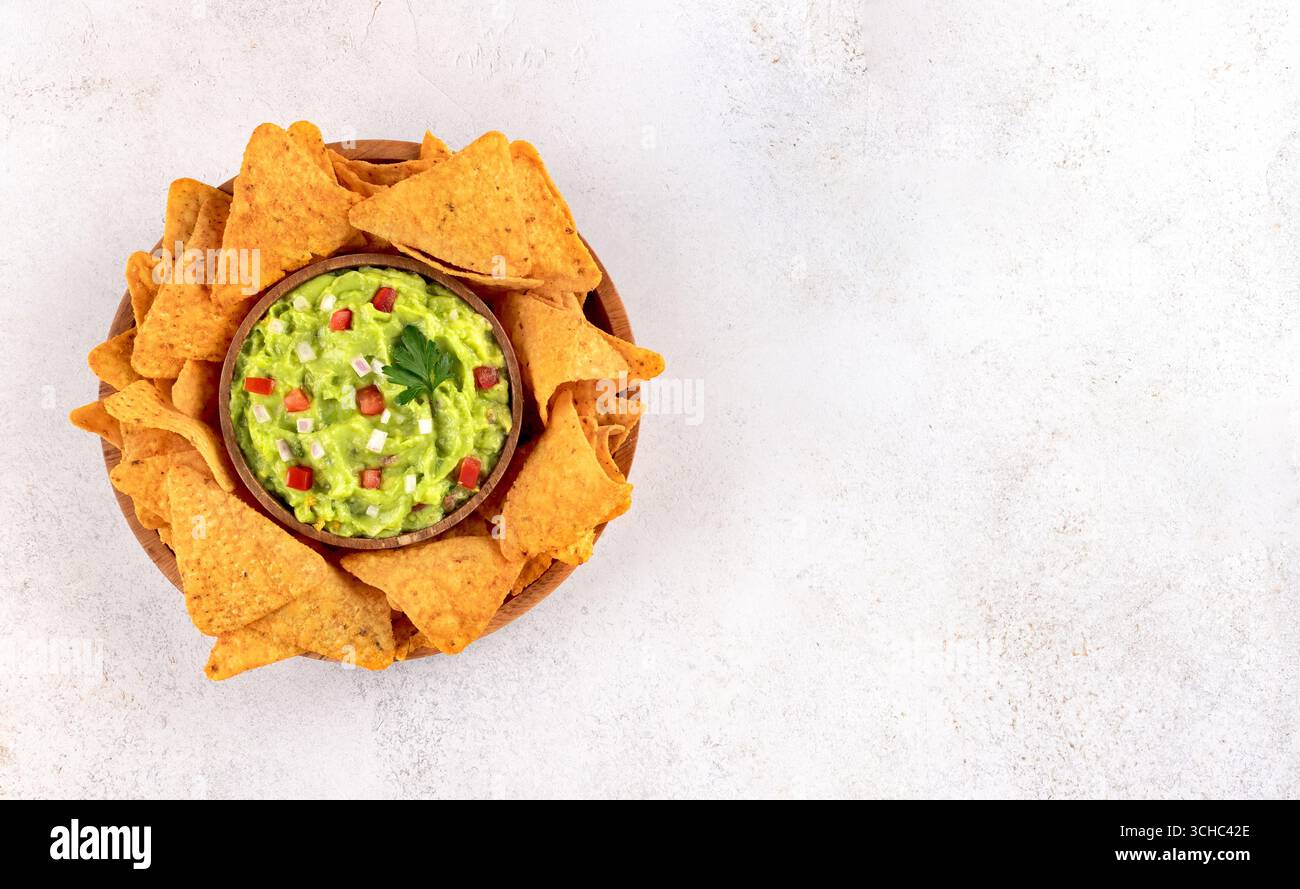 A bowl of guacamole with crispy nachos on a light background. Perfect for a party appetize. Mexican food. Stock Photo