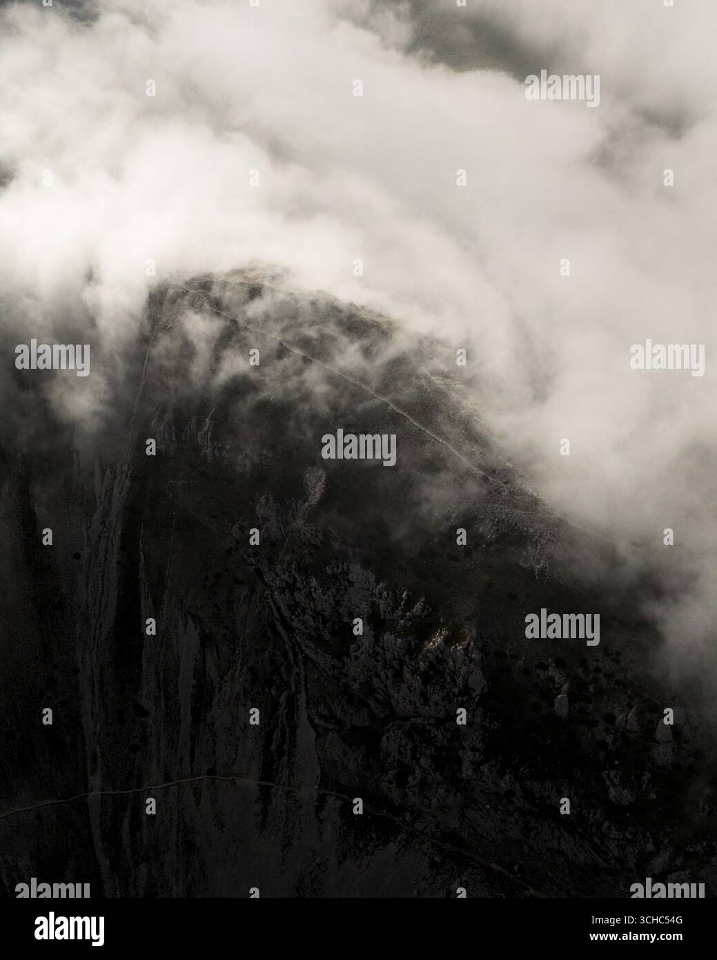 Aerial view of a mountain peak shrouded in ethereal mist and cloud, its ...