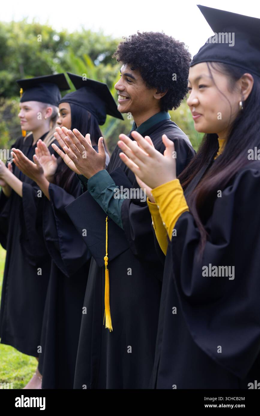 Graduating students in caps and gowns clapping outdoors, celebrating ...