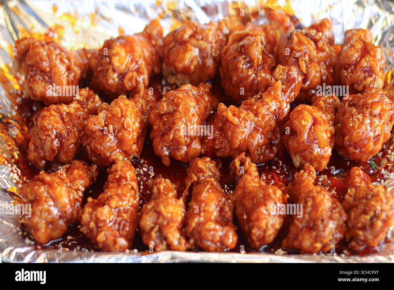 Thai spicy caramel fried chicken wings on foil tray, golden brown and glossy with sweet spicy glaze, authentic Asian street food scene. Stock Photo