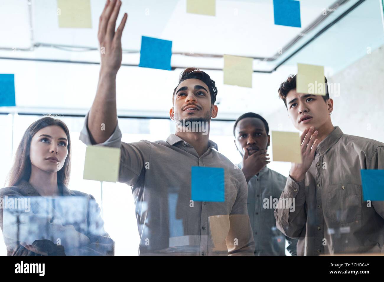 Diverse colleagues brainstorming using sticky notes on glass wall Stock Photo