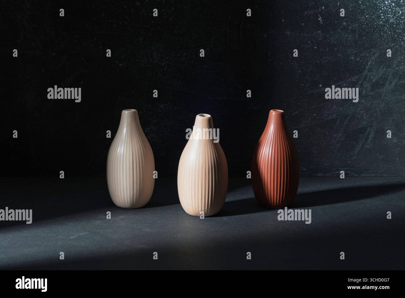 Three ceramic vases on black background in the light. Stock Photo
