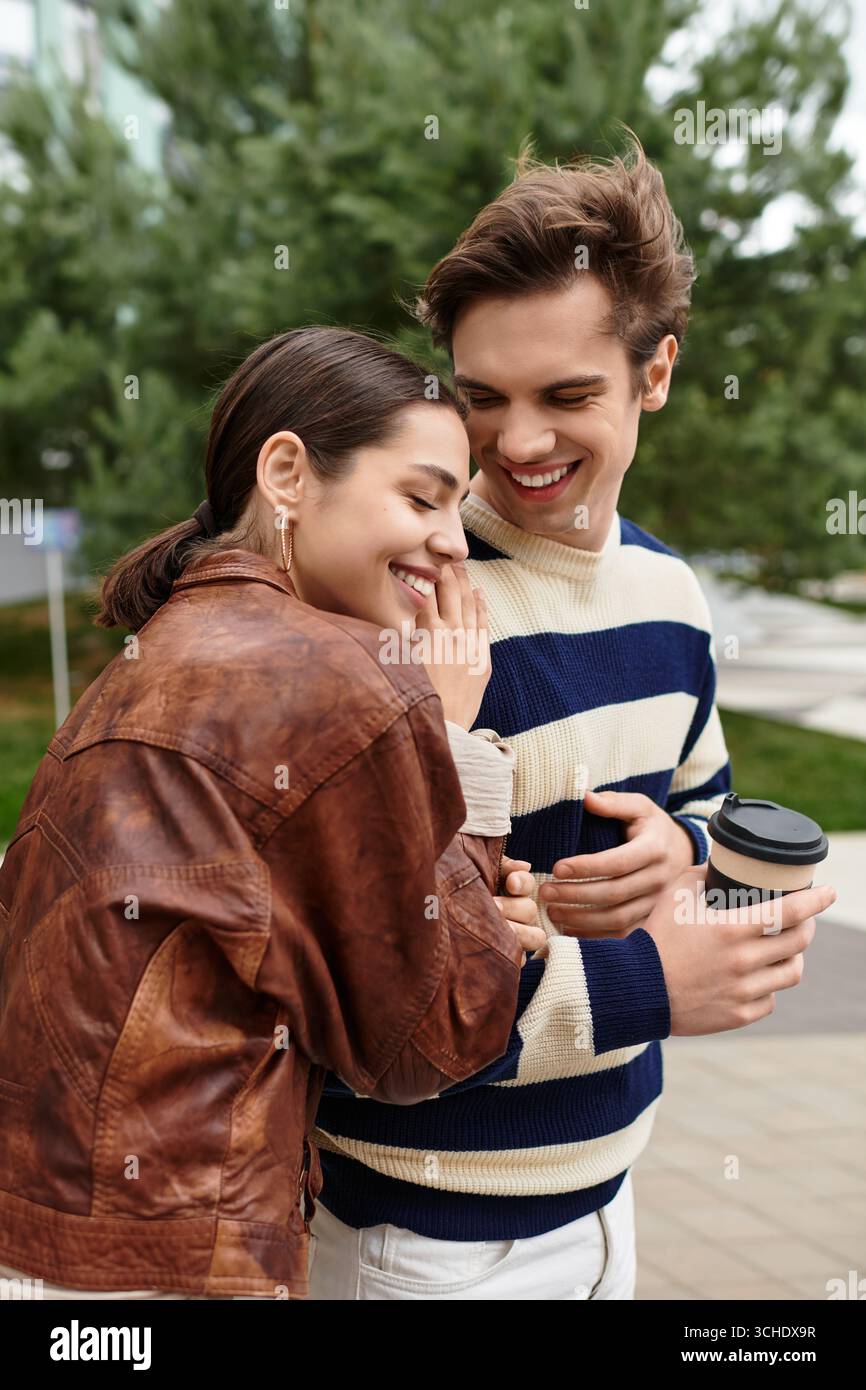 Two young lovers share a joyful embrace while sipping coffee in a natural setting. Stock Photo