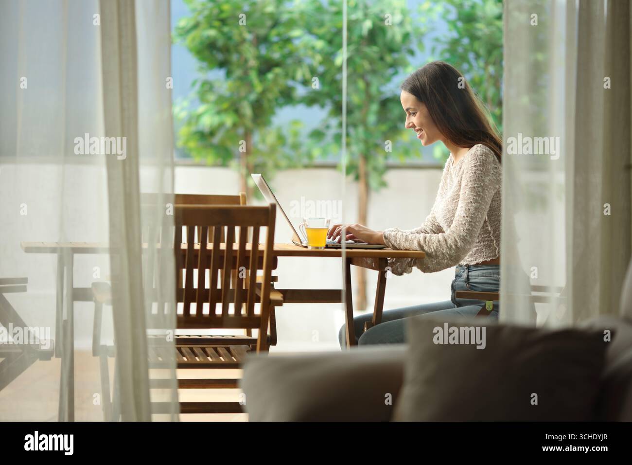 Happy woman using laptop sitting in a terrace in a house outdoors Stock Photo