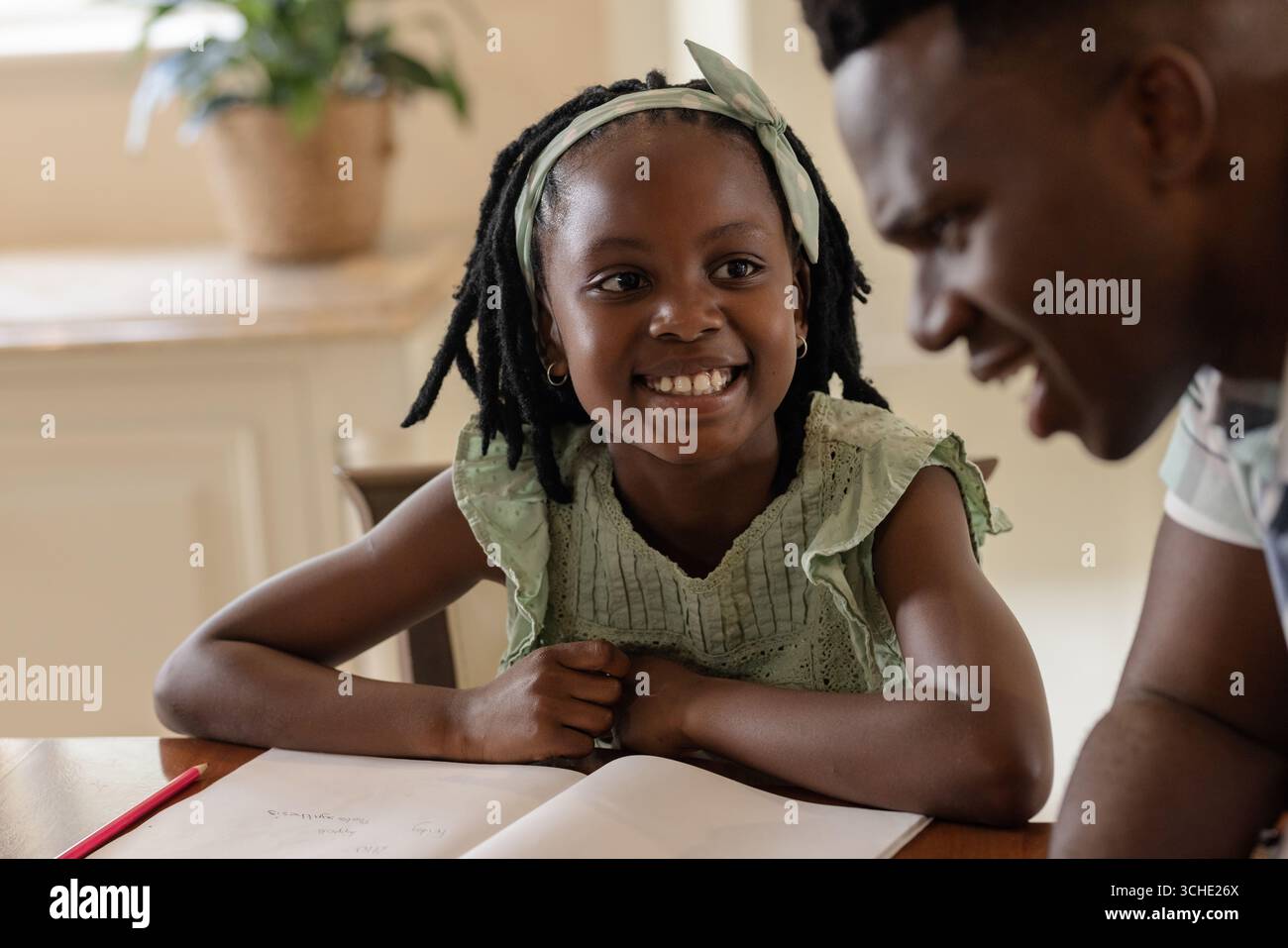 African American girl smiling while doing homework with father at home ...