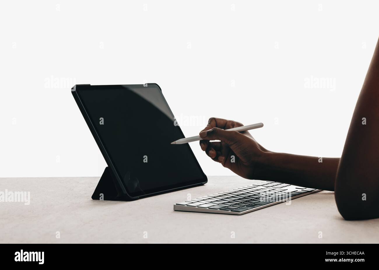 A closeup view of a person interacting with a digital tablet using a stylus. The workspace includes a keyboard and is minimalistic, emphasizing techno Stock Photo