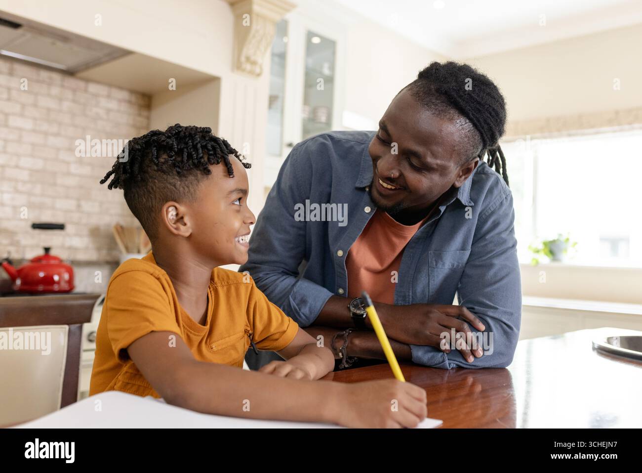 Helping son with homework, African American father smiling warmly at kitchen table Stock Photo