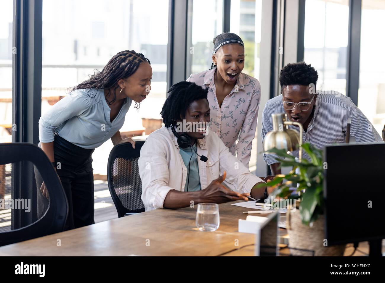Diverse team collaborating enthusiastically around computer in modern office setting Stock Photo