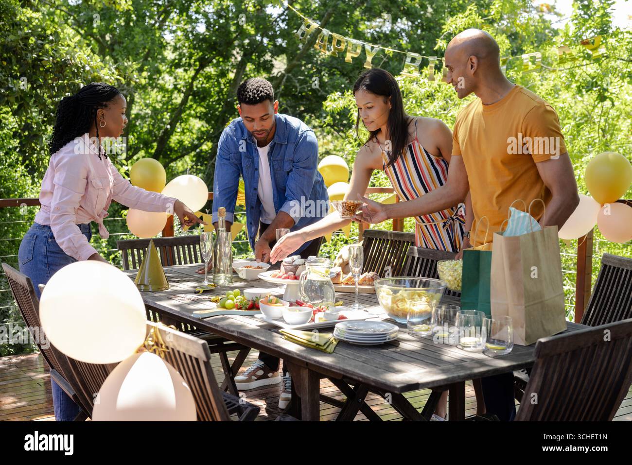Diverse friends enjoying outdoor birthday party, setting table with food and decorations Stock Photo
