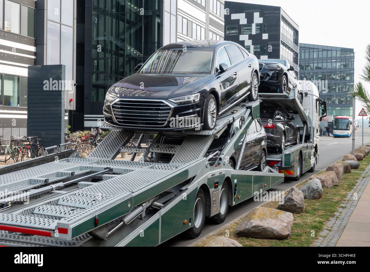 Car carrier truck deliver new auto batch seen from behind in front of modern office buildings. Stock Photo