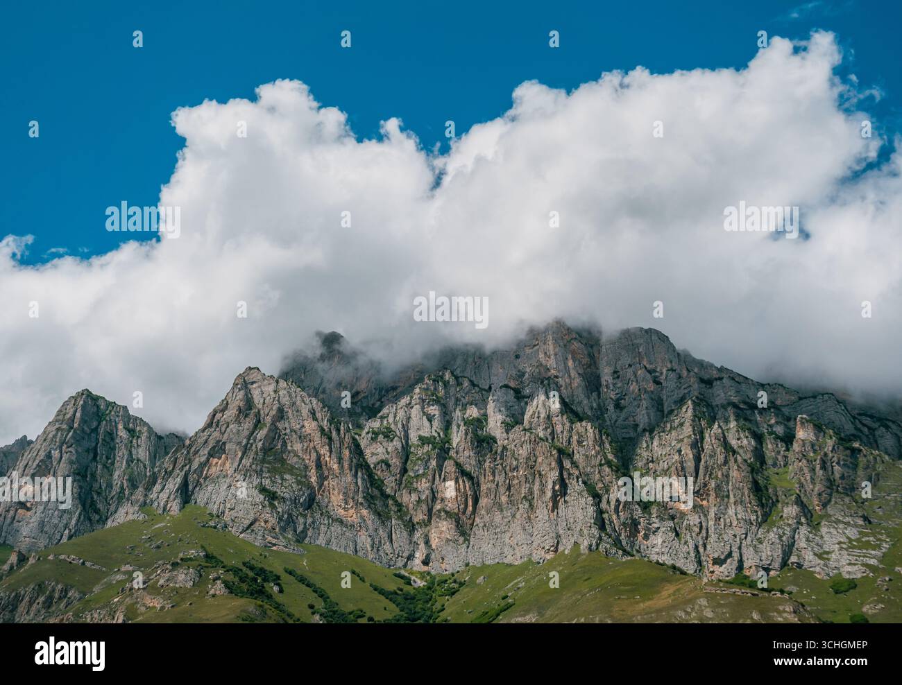 Majestic mountain peaks shrouded in clouds against a vibrant blue sky ...