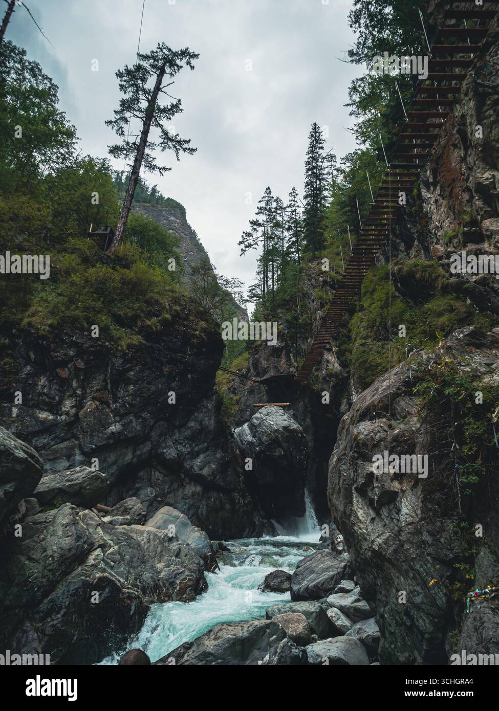 Water rushes over smooth stones at the base of rugged cliffs, while a ...
