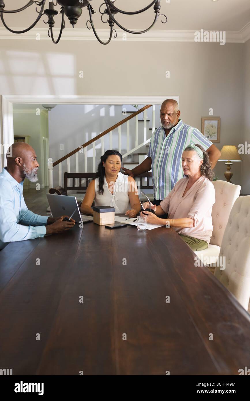 Seniors discussing plans around table, using tablet and notebook at home Stock Photo