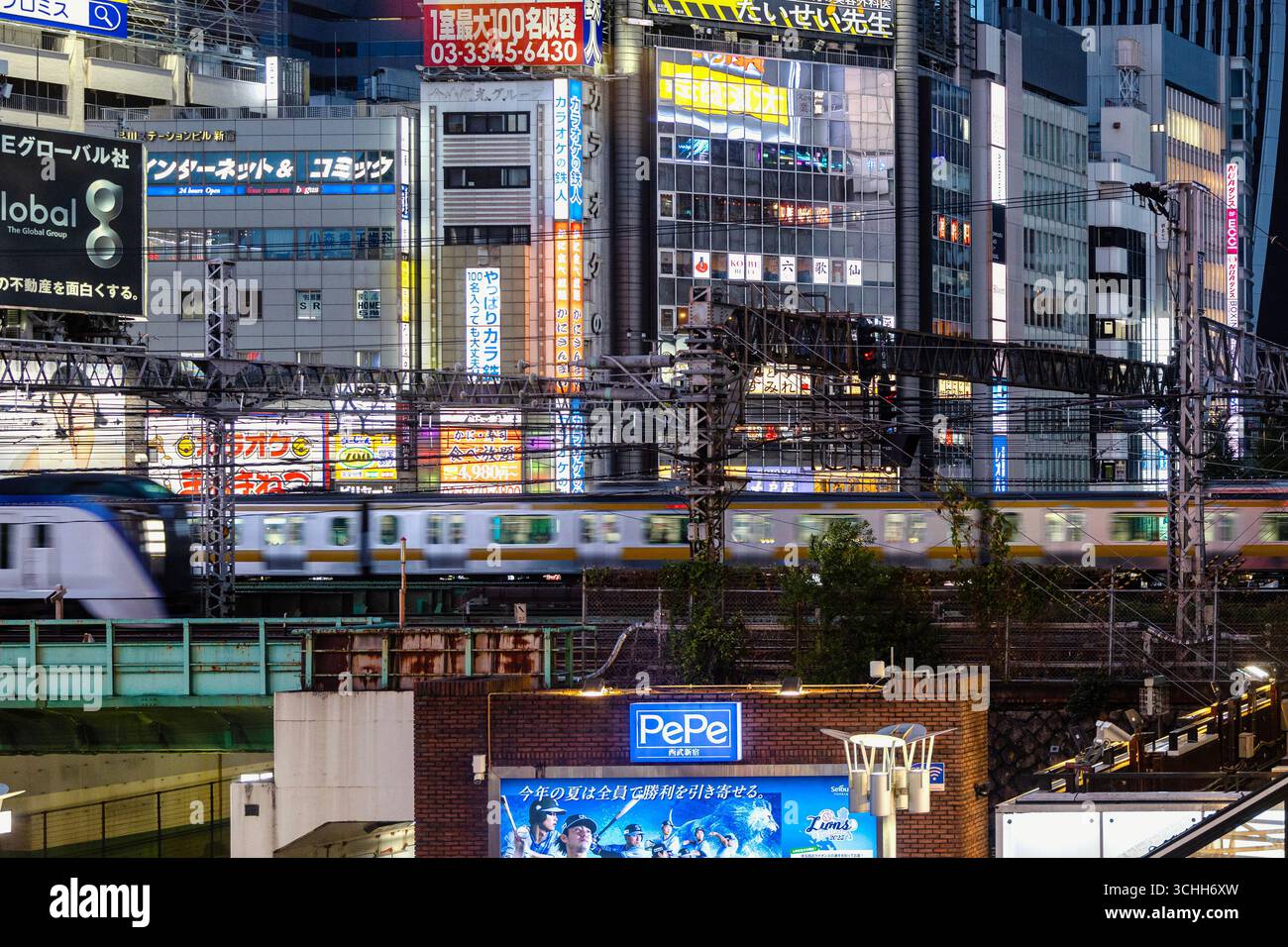 Train coming out of Shinjuku station at night, with buildings lit up in neon lights - Stock Image